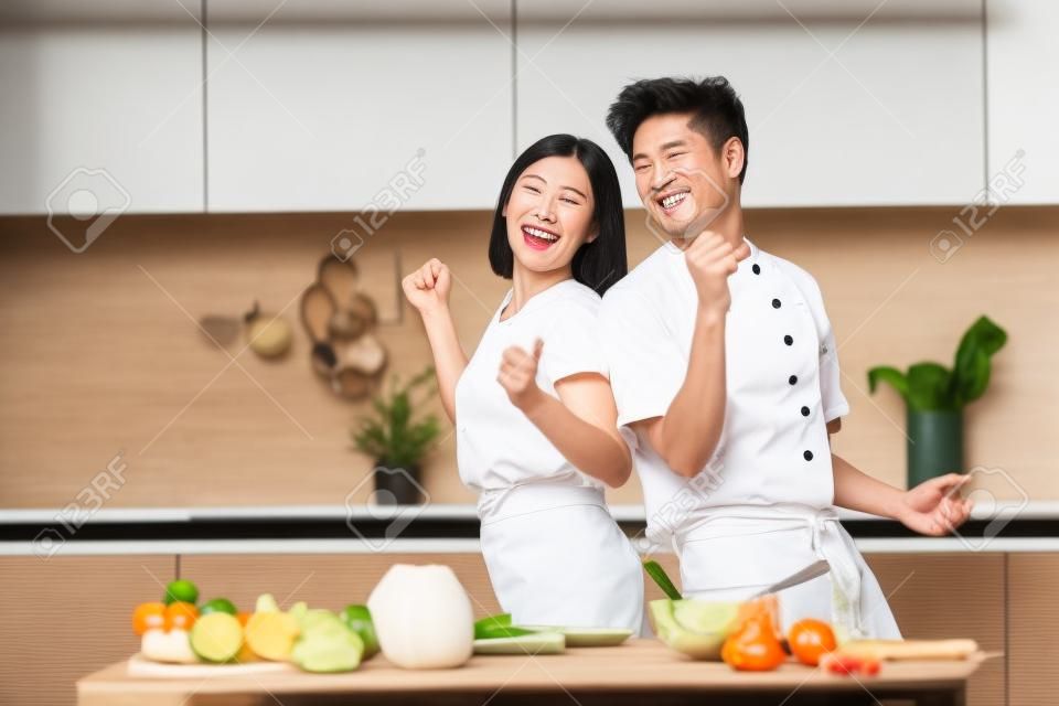 Geniet van koken. Vrolijke Aziatische paar dansen voorbereiding diner en hebben plezier in keuken thuis. gelukkig familie weekend vrije tijd, voedsel voorbereiding en recepten, voeding concept. lege ruimte voor tekst