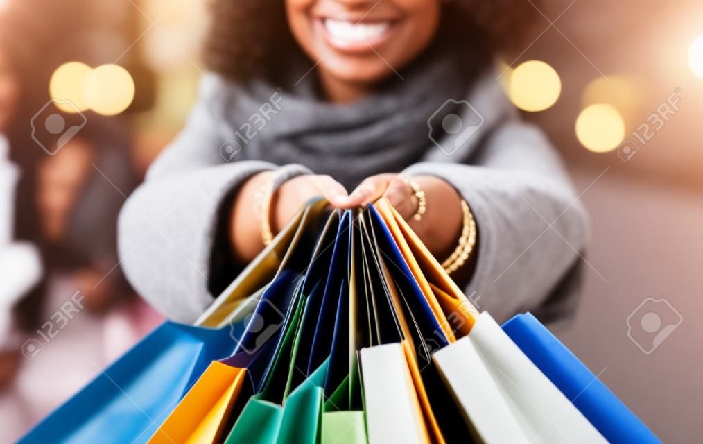 Discount, Sale And Consumerism Concept. Closeup of smiling african american woman holding many shopping bags and showing it to camera. Excited black female shopaholic carrying purchases