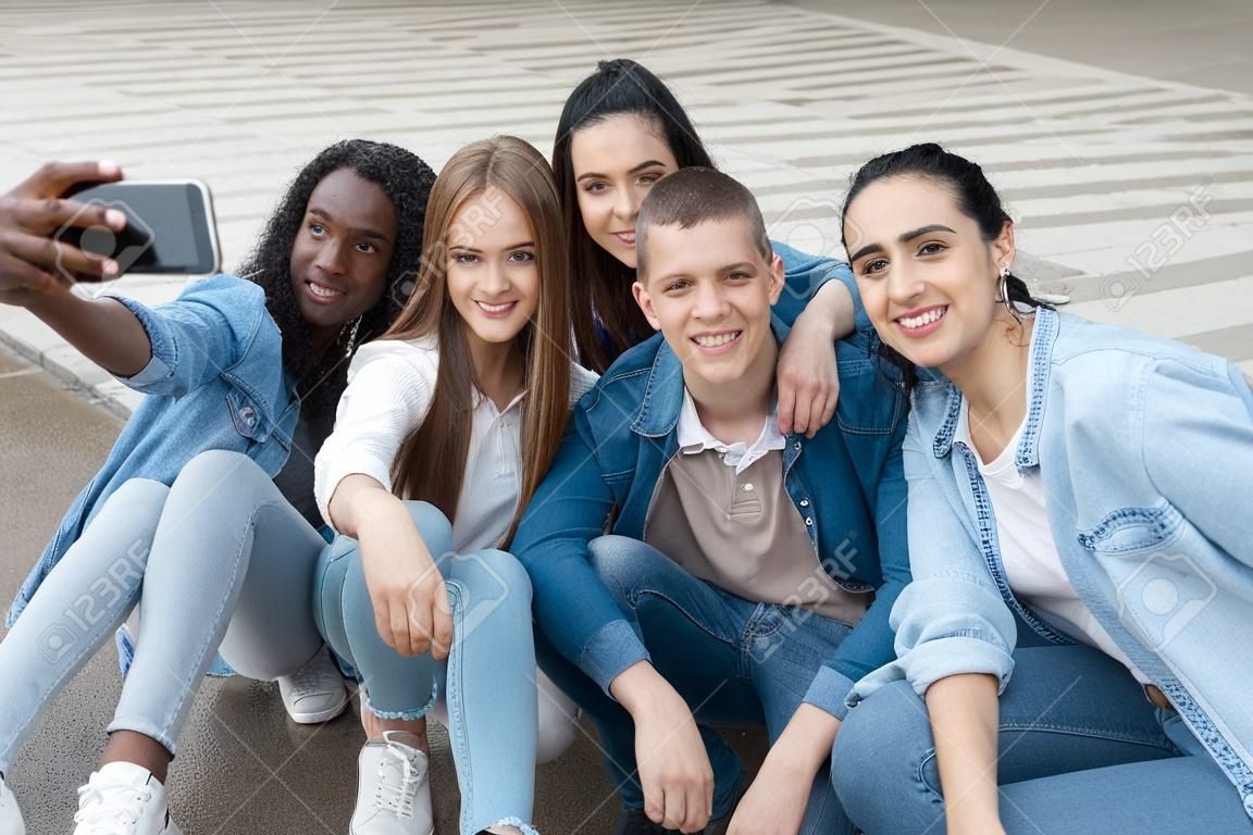 Cinq amis multiraciaux prenant un selfie avec un téléphone à l'extérieur