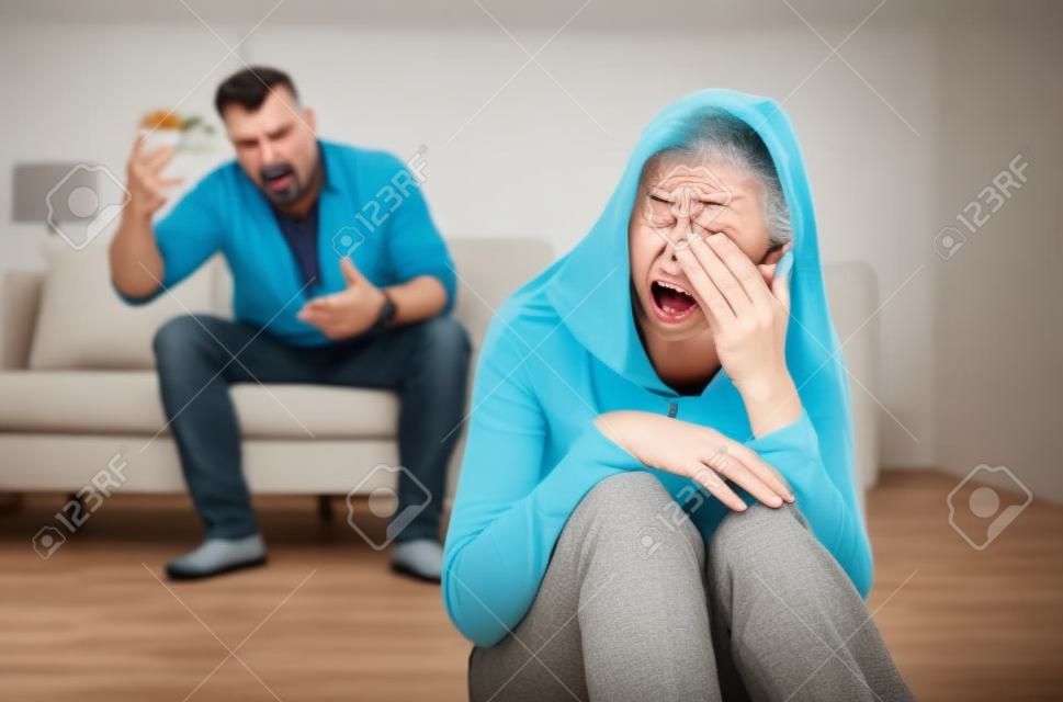 Homme mûr abusant de sa femme déprimée, criant, humiliant et menaçant, femme d'âge moyen pleurant à la maison