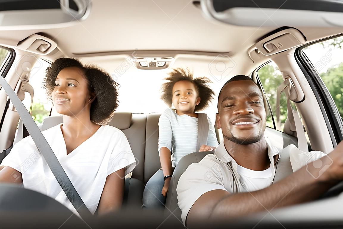 Família americana africana feliz que conduz o automóvel novo que tem passeio ao ar livre