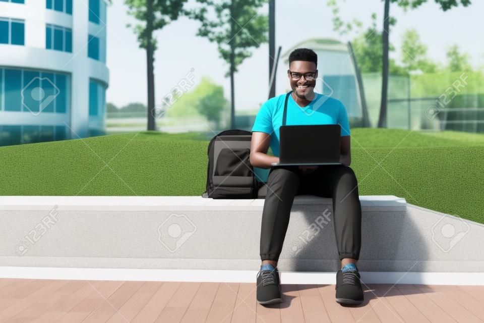 원격 교육 개념입니다. 야외에 앉아 교육 웹 세미나를 보는 노트북을 가진 흑인 남성 학생