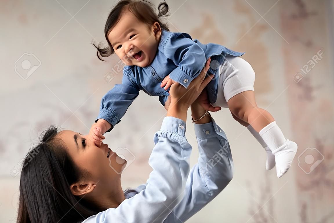 Asian Mother Playing With Baby Lifting Infant In Arms Indoor