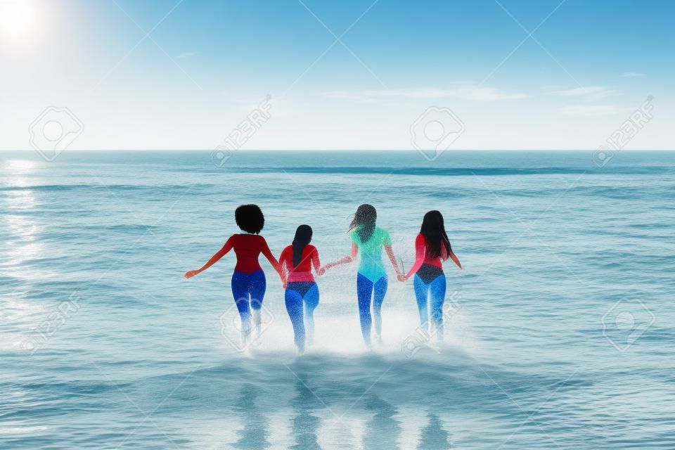 Rückansicht einer Gruppe verschiedener Freundinnen, die beim gemeinsamen Laufen am Strand Wasser planschen, freier Platz