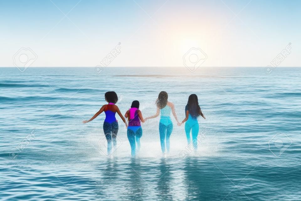 Rückansicht einer Gruppe verschiedener Freundinnen, die beim gemeinsamen Laufen am Strand Wasser planschen, freier Platz