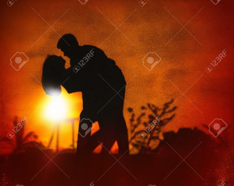 Silhouetten van het knuffelen paar tegen de zonsondergang hemel. Foto met vintage stemming