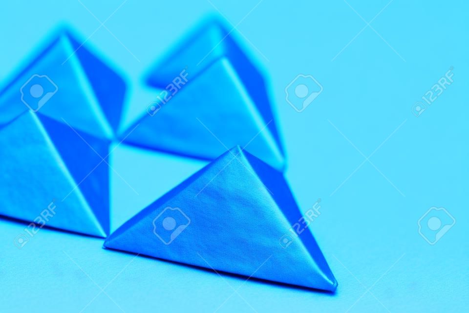 Handmade 3d origami paper triangle on blue background close up, selective focus