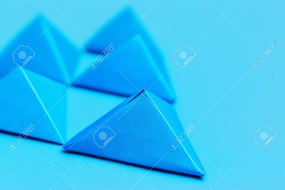 Handmade 3d origami paper triangle on blue background close up, selective focus