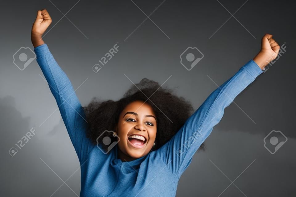 Portrait of a cheerful young black woman smiling with arms raised