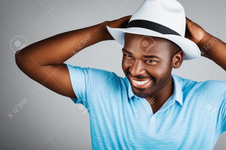 Close up retrato de un hombre afroamericano despreocupado y sonriente con sombrero sobre fondo blanco