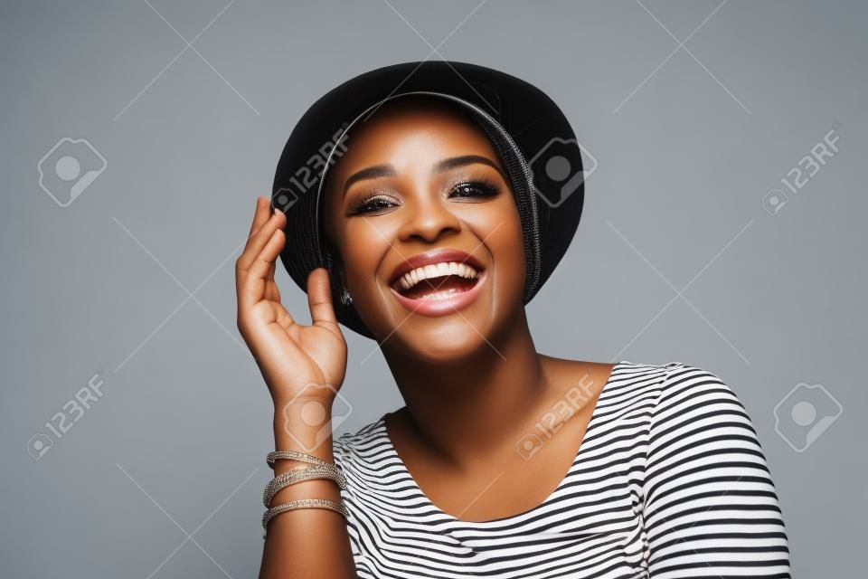 Close up Portrait einer attraktiven jungen schwarzen Frau lächelnd mit Hut vor weißem Hintergrund