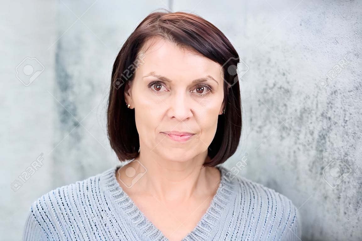 Close up portrait of a beautiful older woman with brown hair standing against gray background