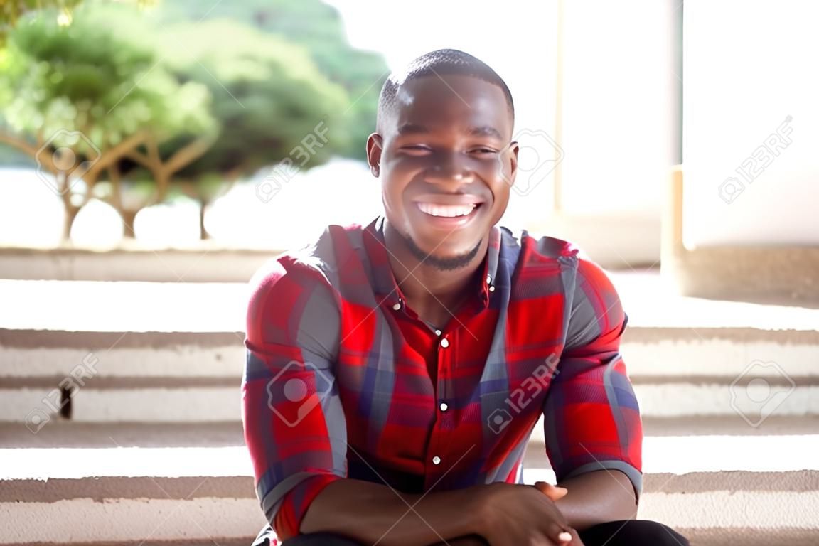 Sluit het portret van de glimlachende jonge Afrikaan die buiten op treden zit