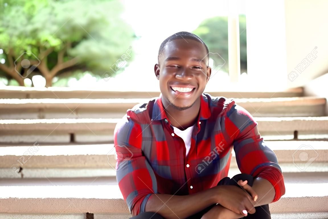 Sluit het portret van de glimlachende jonge Afrikaan die buiten op treden zit