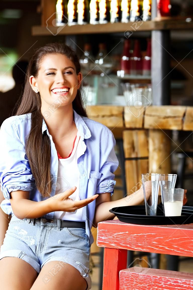 Ritratto di giovane server femminile ridendo con vassoio di bevande