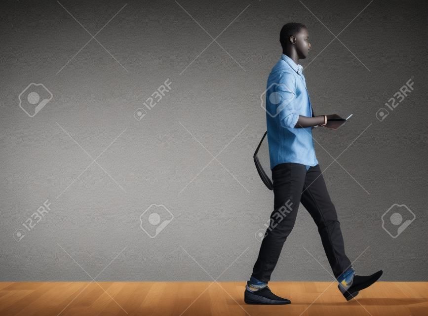 Profile portrait of black male student walking with tablet