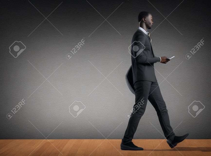 Profile portrait of black male student walking with tablet