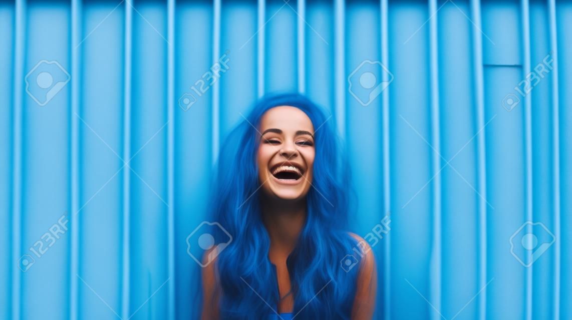 Portrait of a young beautiful woman laughing against blue wooden wall.