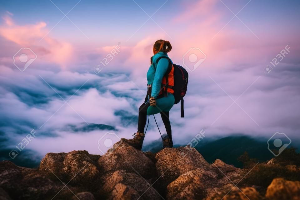 Ein Wandermädchen mit Rucksack auf dem Rücken beobachtet den Morgen vom Gipfel des Berges aus