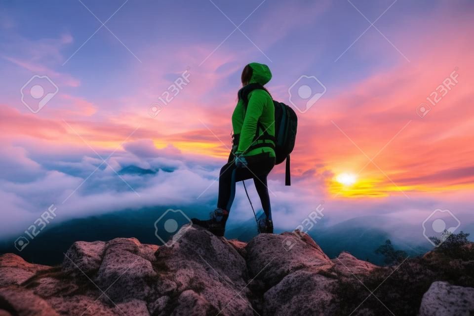 Ein Wandermädchen mit Rucksack auf dem Rücken beobachtet den Morgen vom Gipfel des Berges aus