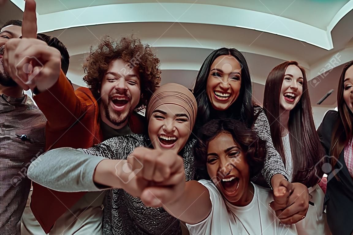 In a heartwarming scene, a diverse group of friends gathers around a television, radiating joy and unity as they collectively witness and celebrate a joyful event together.