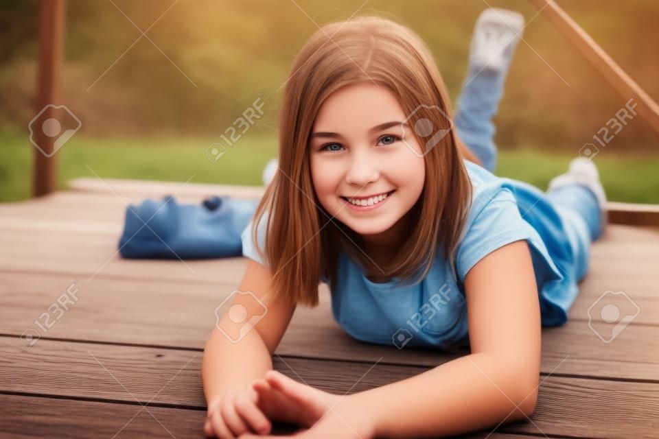 Adorable smiling teen girl lying on her stomach on a wooden bridge