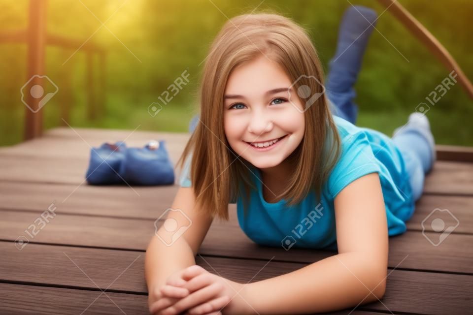 Adorable smiling teen girl lying on her stomach on a wooden bridge