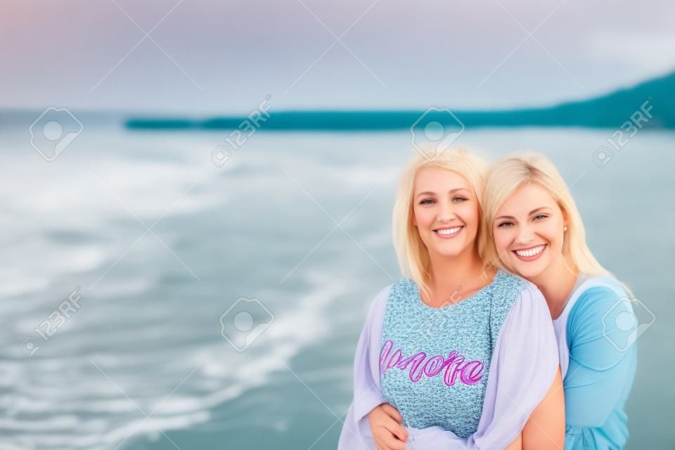 Adult daughter hugs mom on the sea shore and both are smiling