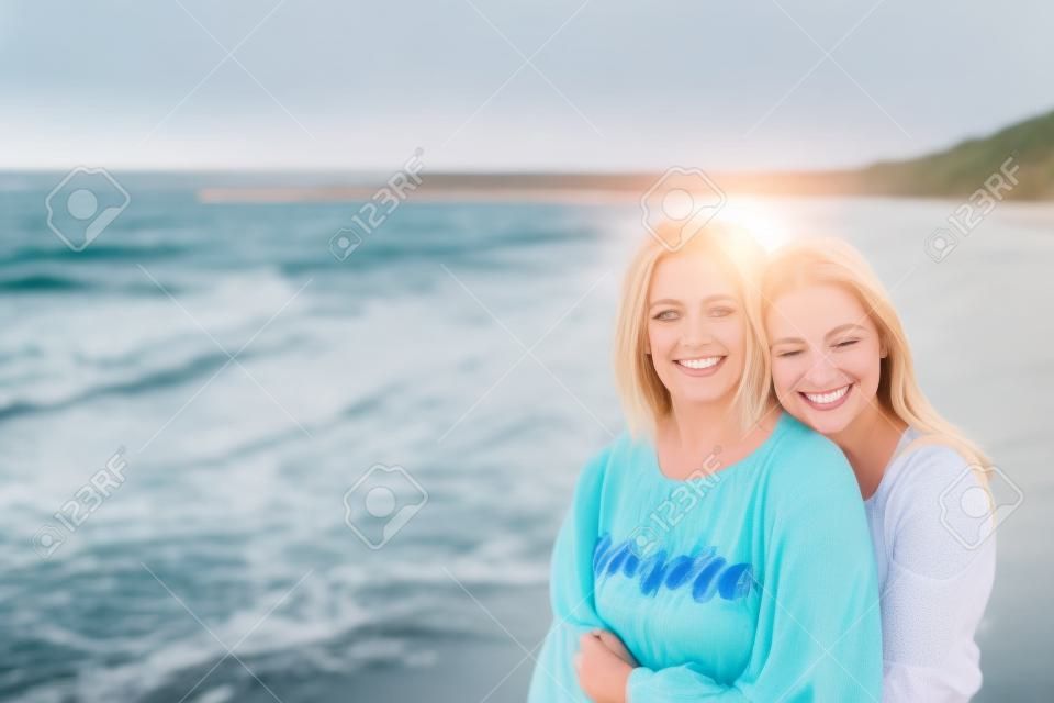 La figlia adulta abbraccia la mamma sulla riva del mare ed entrambe sorridono