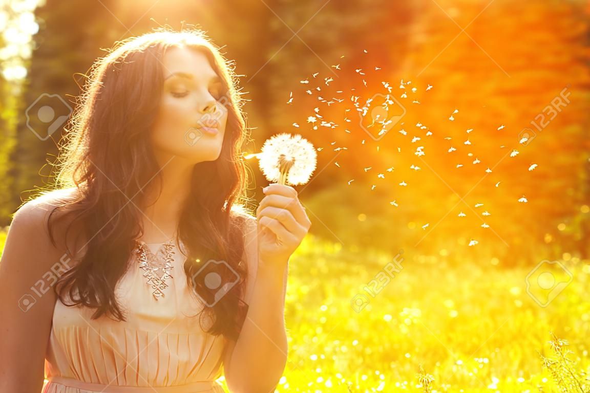 Красивая молодая женщина, дует одуванчика. Модный молодая девушка на закате с цветком