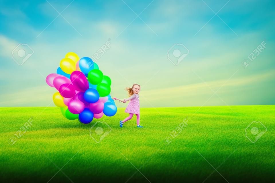 Glückliches kleines Mädchen mit bunten Luftballons auf einer grünen Wiese.