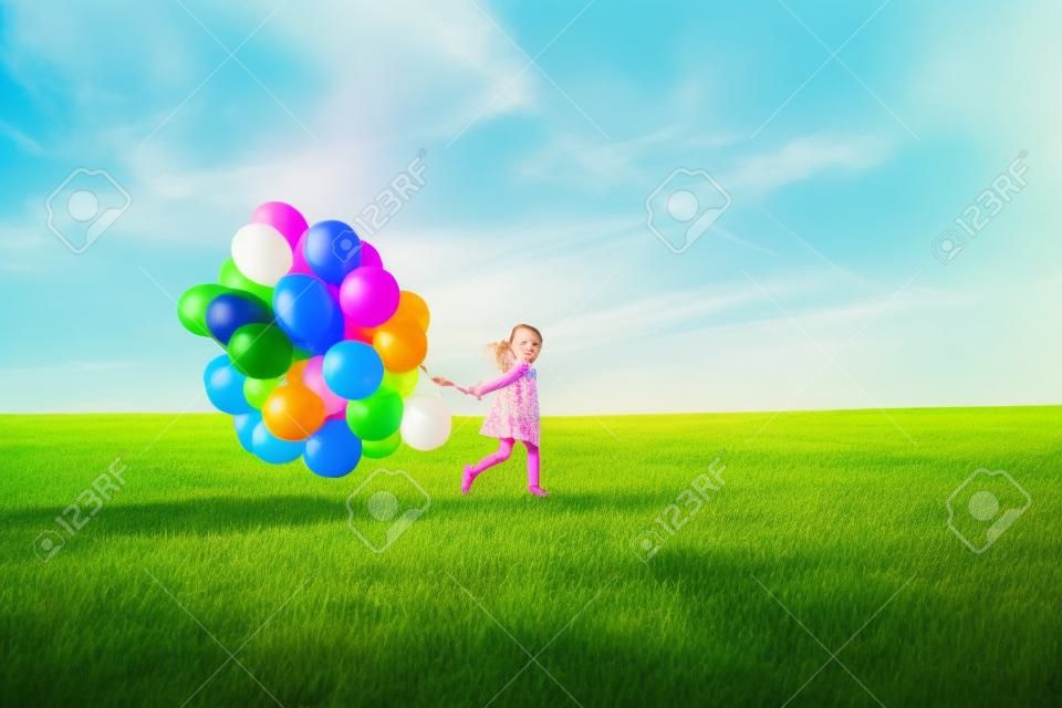Glückliches kleines Mädchen mit bunten Luftballons auf einer grünen Wiese.