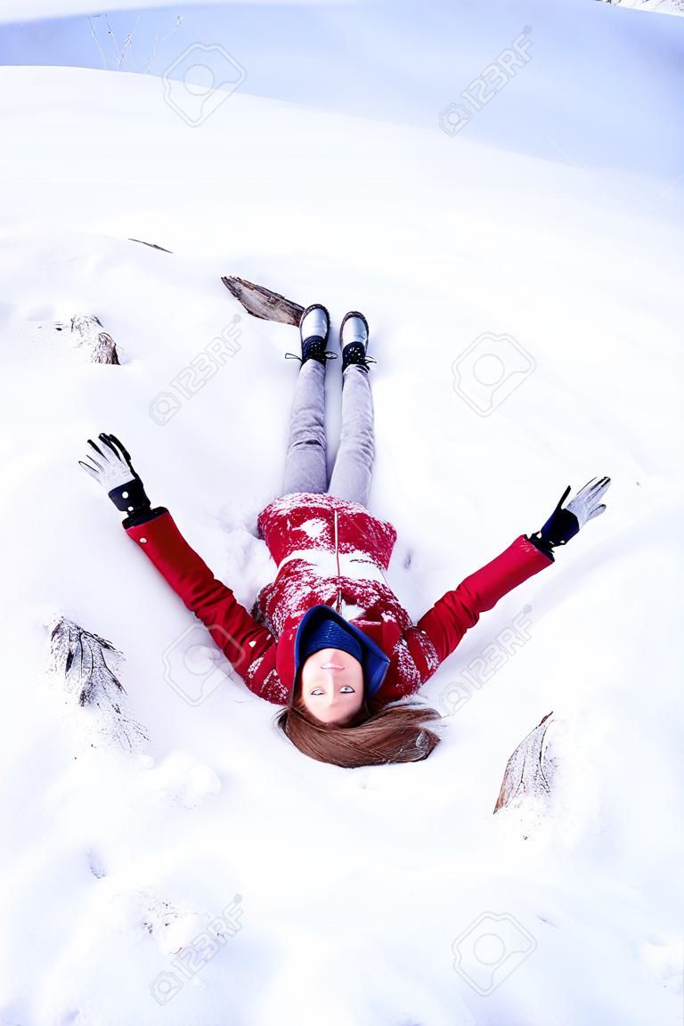 雪の上に横たわる赤いコートを着た若いおかしな女性。冬を楽しむ