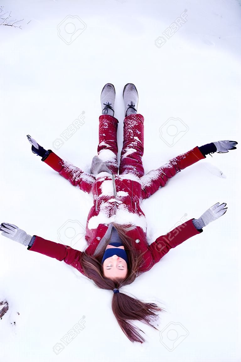 雪の上に横たわる赤いコートを着た若いおかしな女性。冬を楽しむ