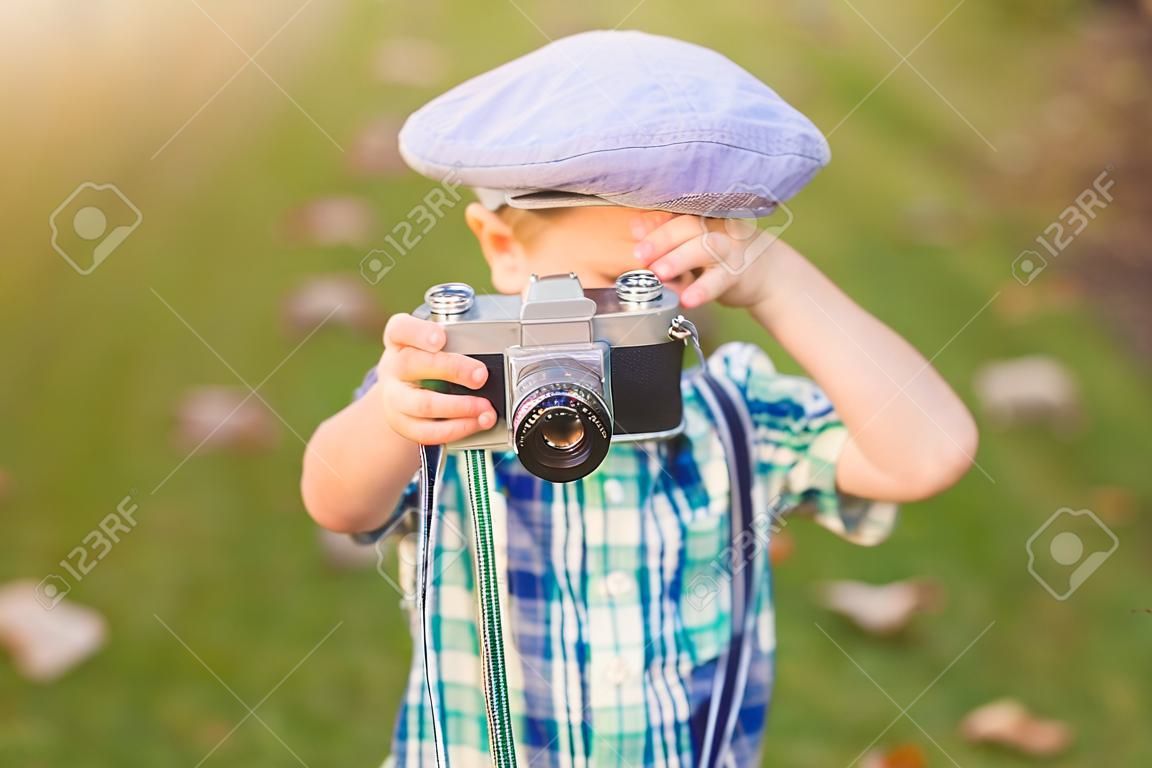 Niño pequeño con un viejo tiroteo de la cámara al aire libre. utilizando una cámara de película retro vintage. Campo de verano.