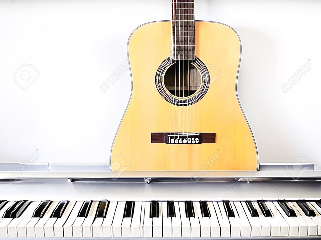 Guitare acoustique sur clavier de piano devant un mur blanc.