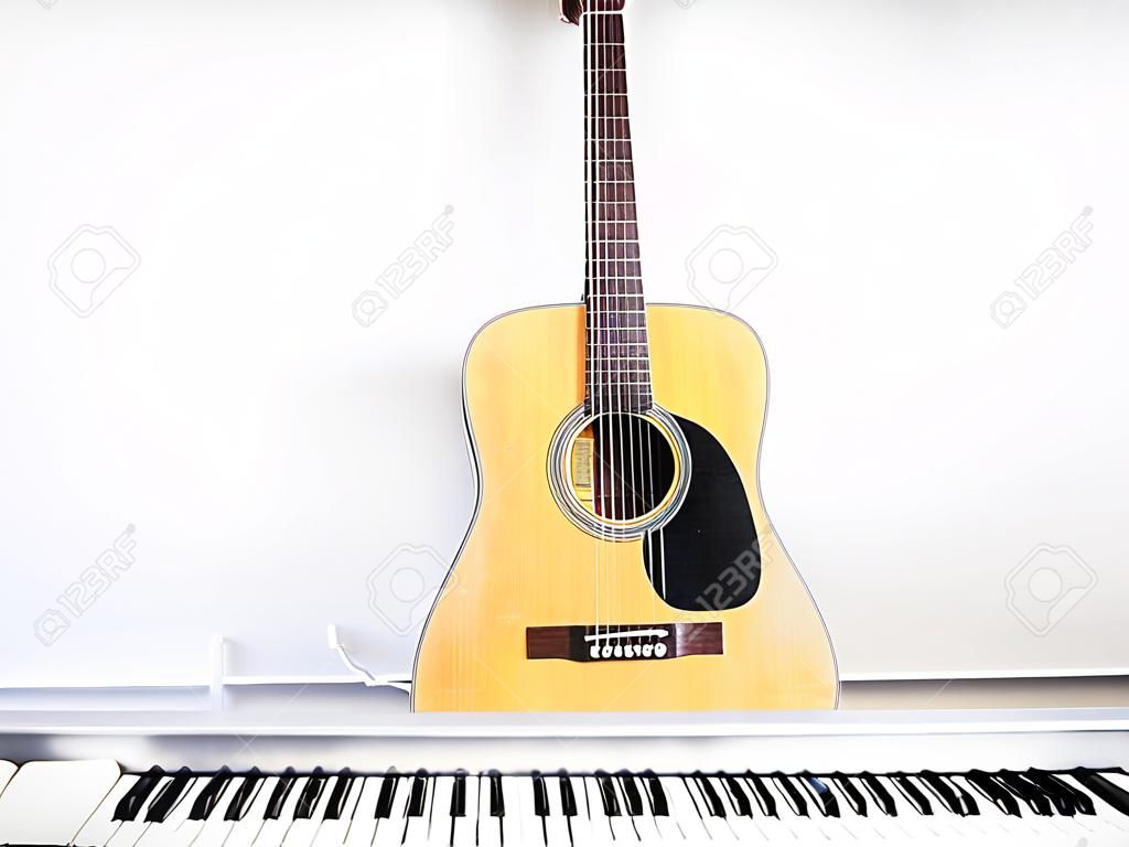 Acoustic guitar on piano keyboard in front of white wall.