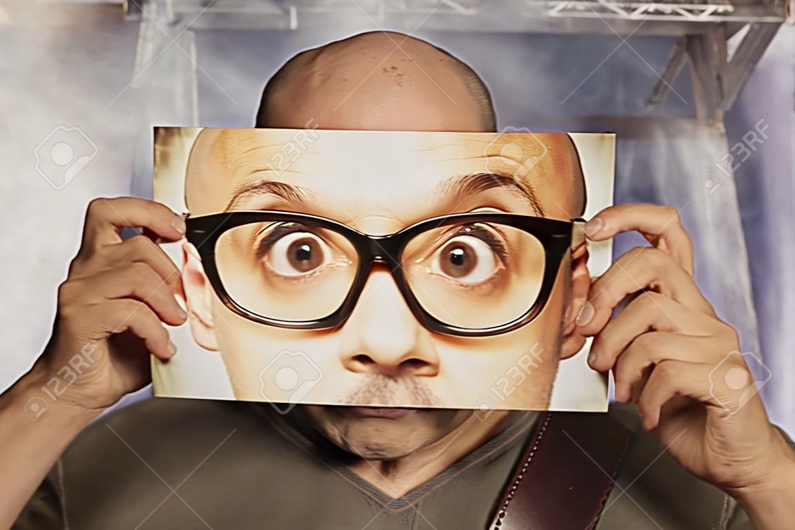 bald man holding a card with a big glasses on it