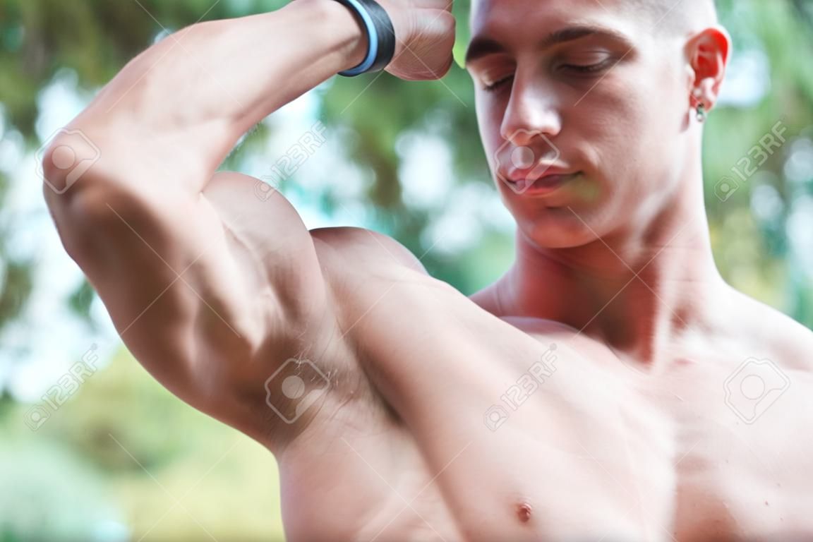 young muscular adult showing off his biceps outdoors. healthy life concept