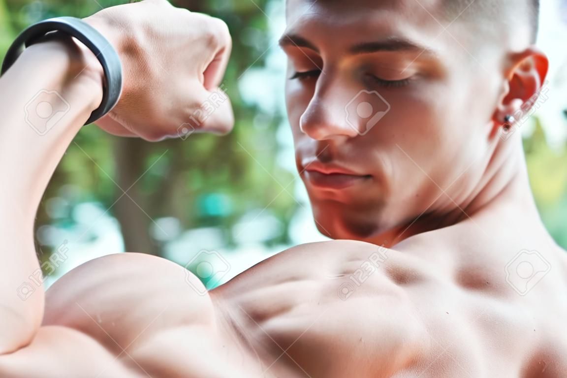 young muscular adult showing off his biceps outdoors. healthy life concept
