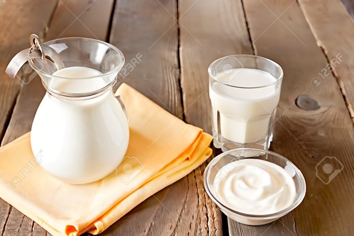 Produtos lácteos frescos de cálcio: leite e creme azedo (iogurte) em guardanapo e mesa de madeira, close up, horizonte, espaço de cópia