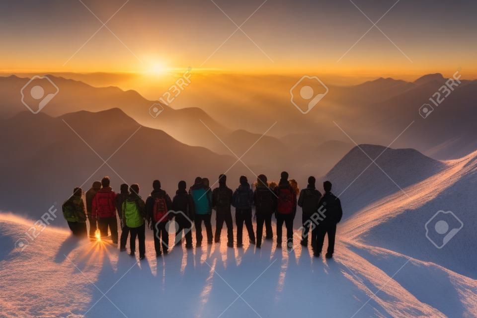 Grupo de personas de pie en la cima de una montaña y mirando el atardecer