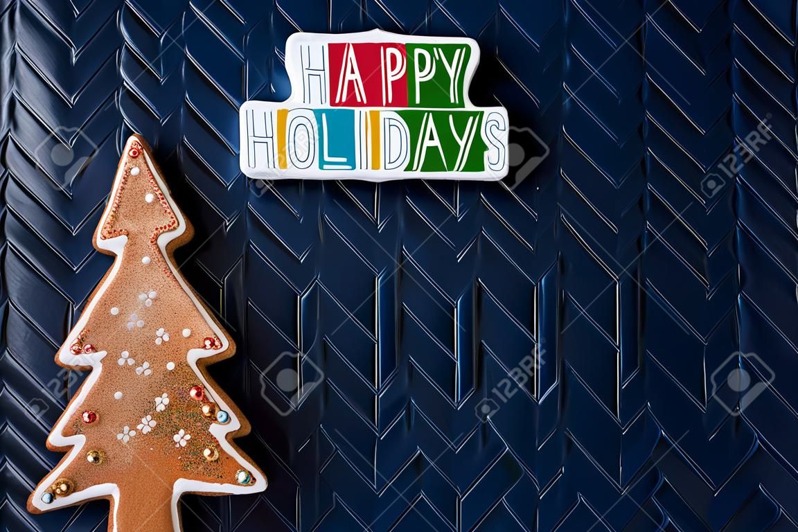 Messaggio di targa di buone feste e un albero di Natale di pan di zenzero glitterato su sfondo blu