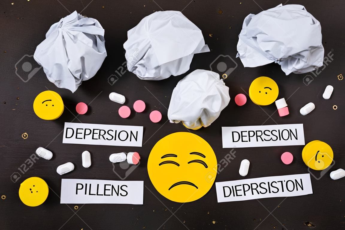 Depression concept. Psychological illness. sad smiley and symptoms of depression and pills on a dark background. view from above