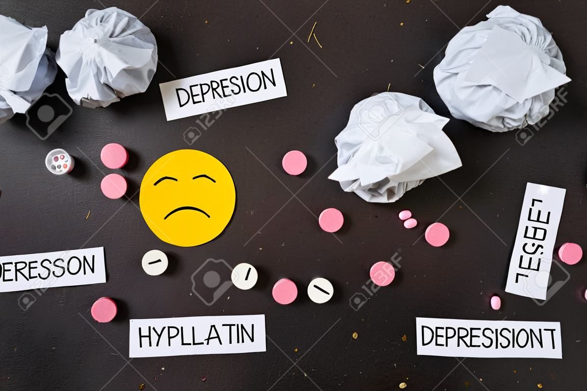 Depression concept. Psychological illness. sad smiley and symptoms of depression and pills on a dark background. view from above