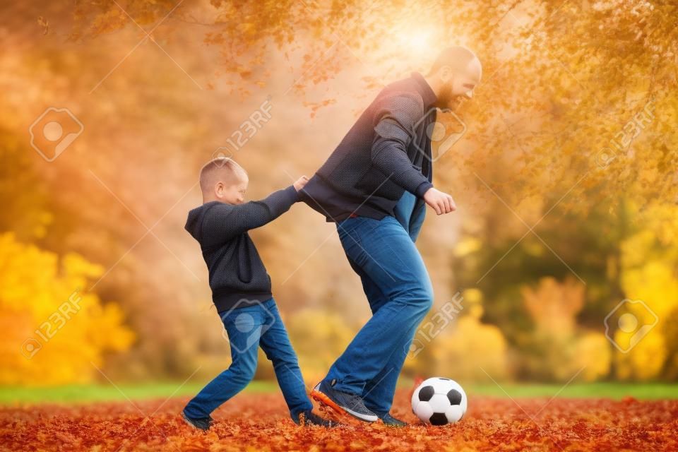 Ojciec i syn grają w piłkę nożną na świeżym powietrzu w słoneczny dzień wśród jesiennych liści.