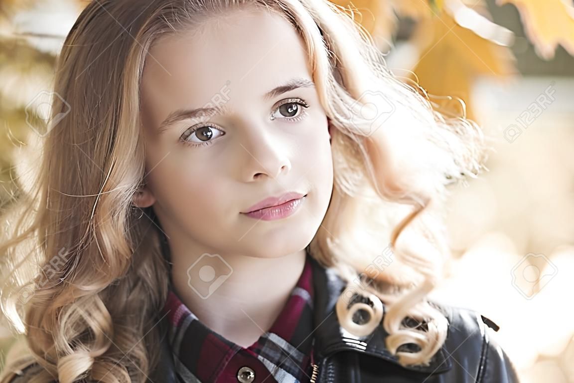 Beautiful blonde teenage girl 12-14 year old wearing leather jacket outdoors. Looking at camera. Autumn season. 