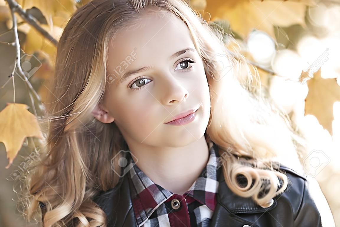 Beautiful blonde teenage girl 12-14 year old wearing leather jacket outdoors. Looking at camera. Autumn season. 