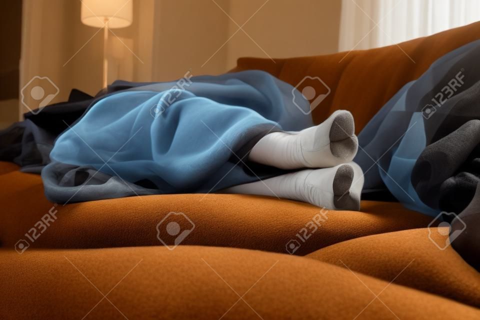Ein Portrait von schwarzen Strumpfhosenfüßen eines Mädchens, während sie auf der Couch im Wohnzimmer unter einer braunen, kuscheligen Decke schläft.