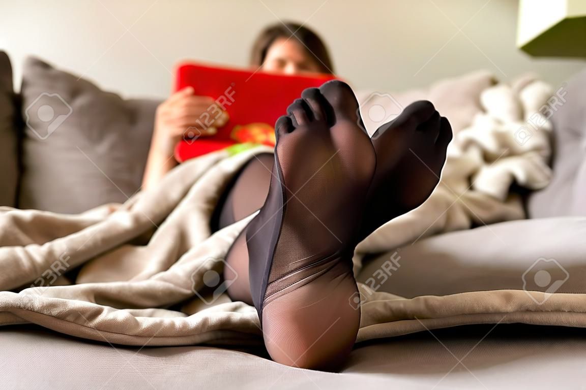 A portrait of a woman's feet wearing black nylon pantyhose or stockings with reinforces toes on a cozy couch in a living room trying to relax after a hard day of work.
